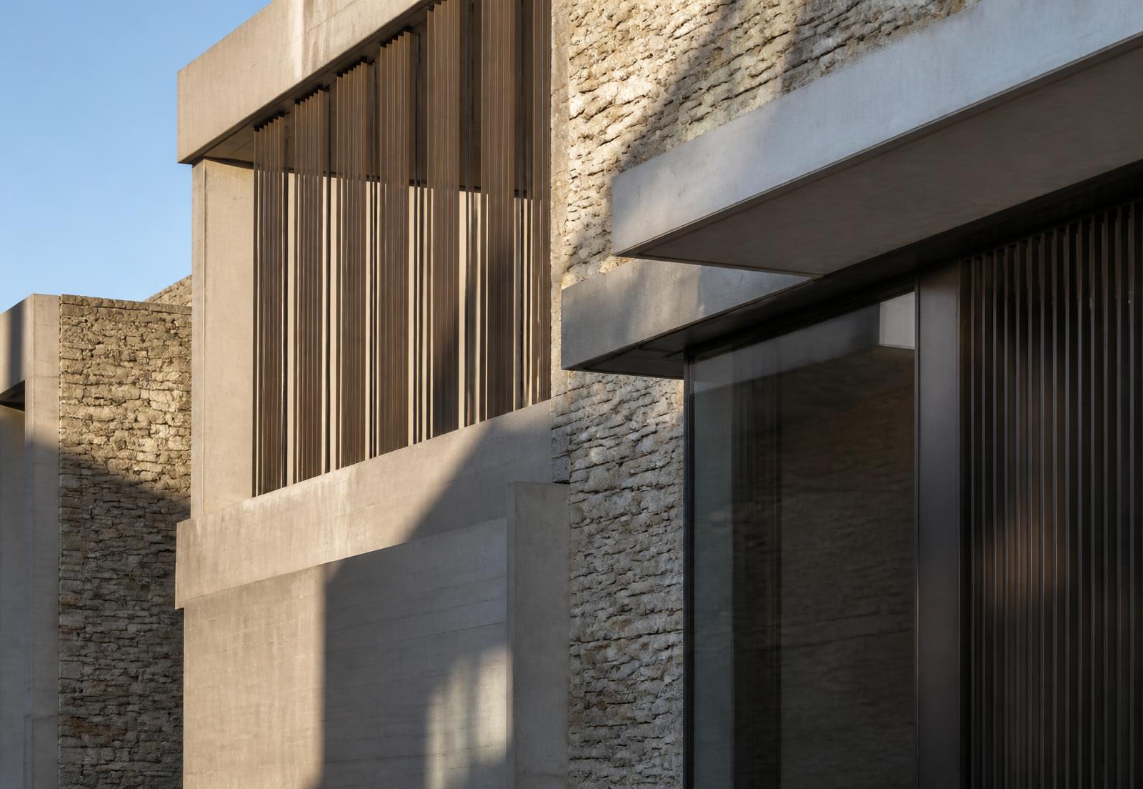 Detalhe de fachada contemporânea em concreto, pedra natural e brises verticais sob luz rasante