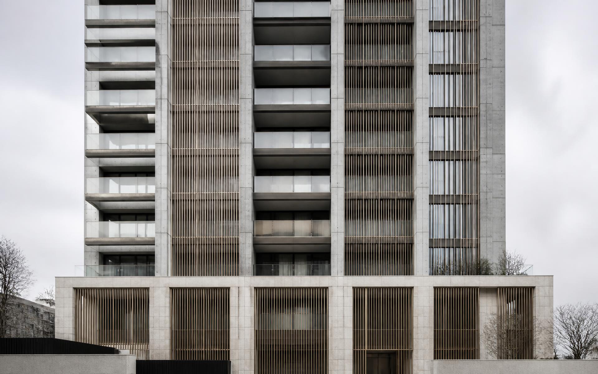 Fachada de edifício residencial contemporâneo em concreto aparente, pedra natural e brises metálicos